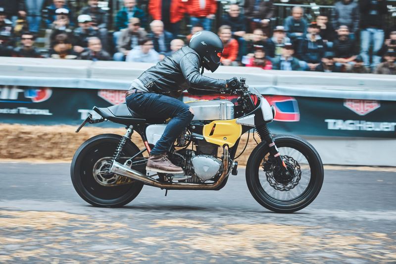 Cafe racer con la tabella gialla tra le balle di fieno, tribuna gremita